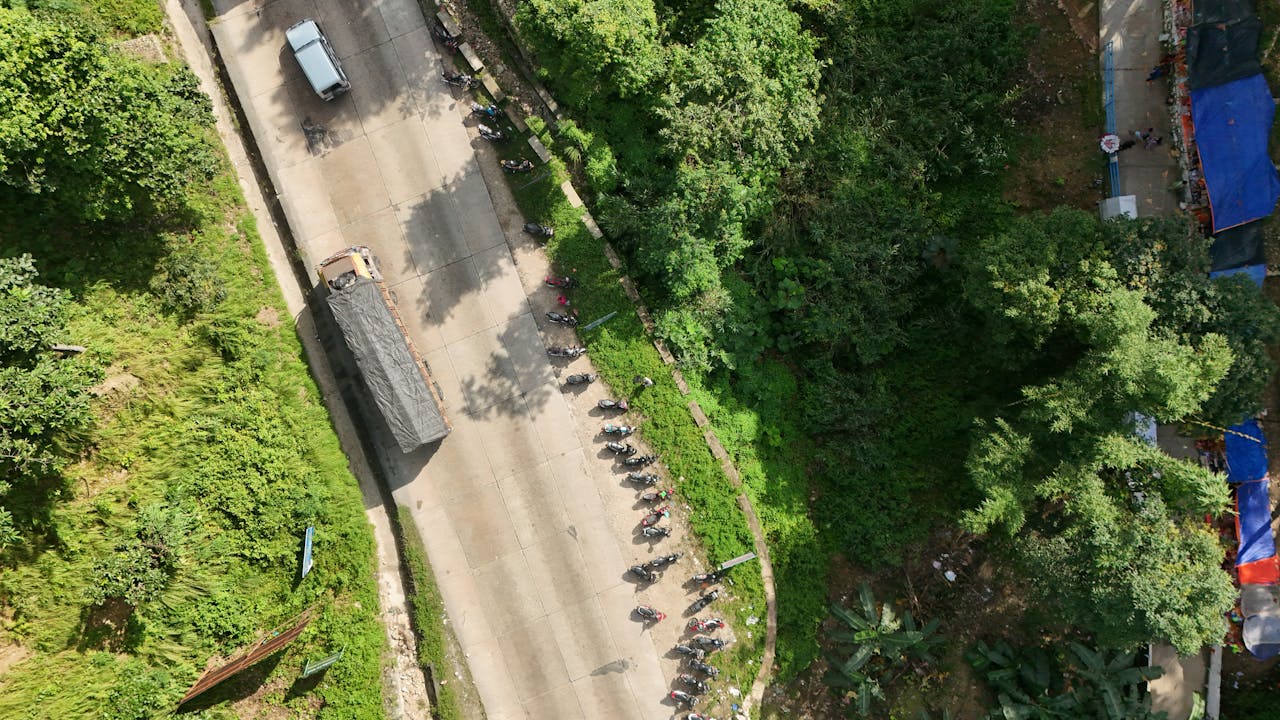 about-02 Aerial shot of a road with parked vehicles surrounded by lush greenery, creating a serene landscape.